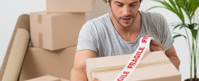 Portrait Of A Young Man Packing Cardboard Box With Fragile Sellotape